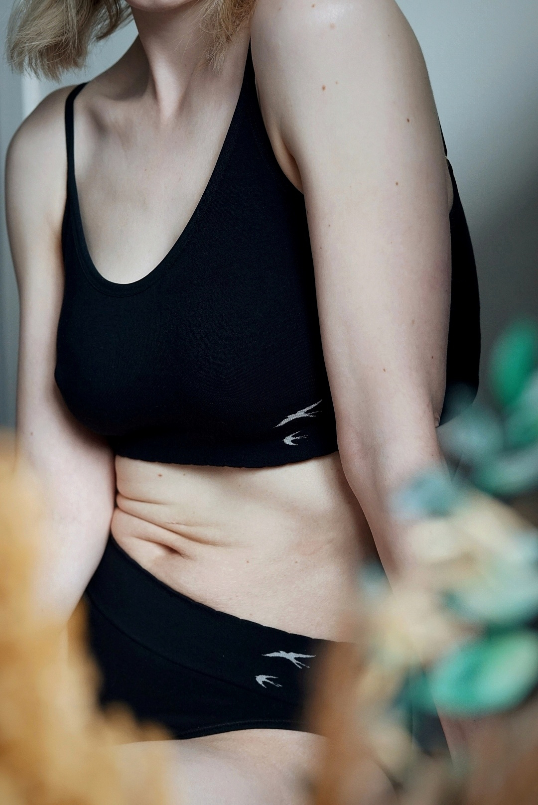 Close up of Amy sitting down wearing a black crop top and pants. You can see her tummy creases.