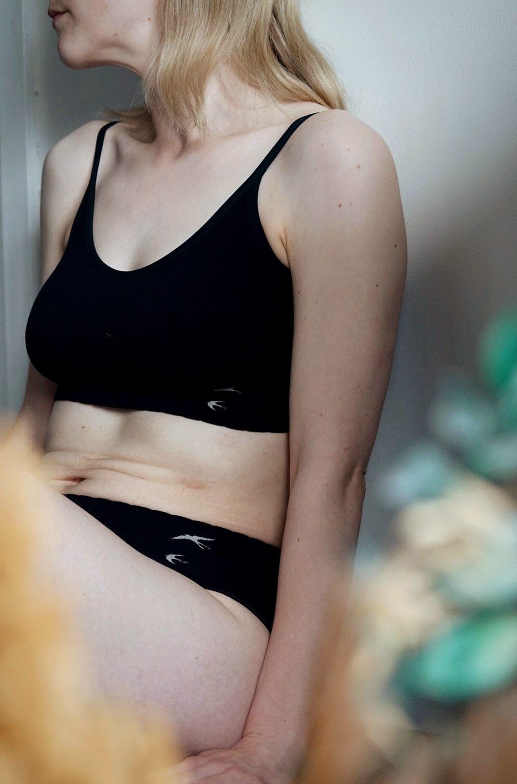 Close up of Amy sitting down wearing a black crop top and pants. You can see her stomach creases.