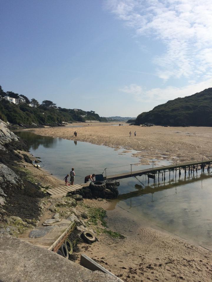 a tidal beach, long sandy beach with a waterway running down the side, bridge leading to a cliff side