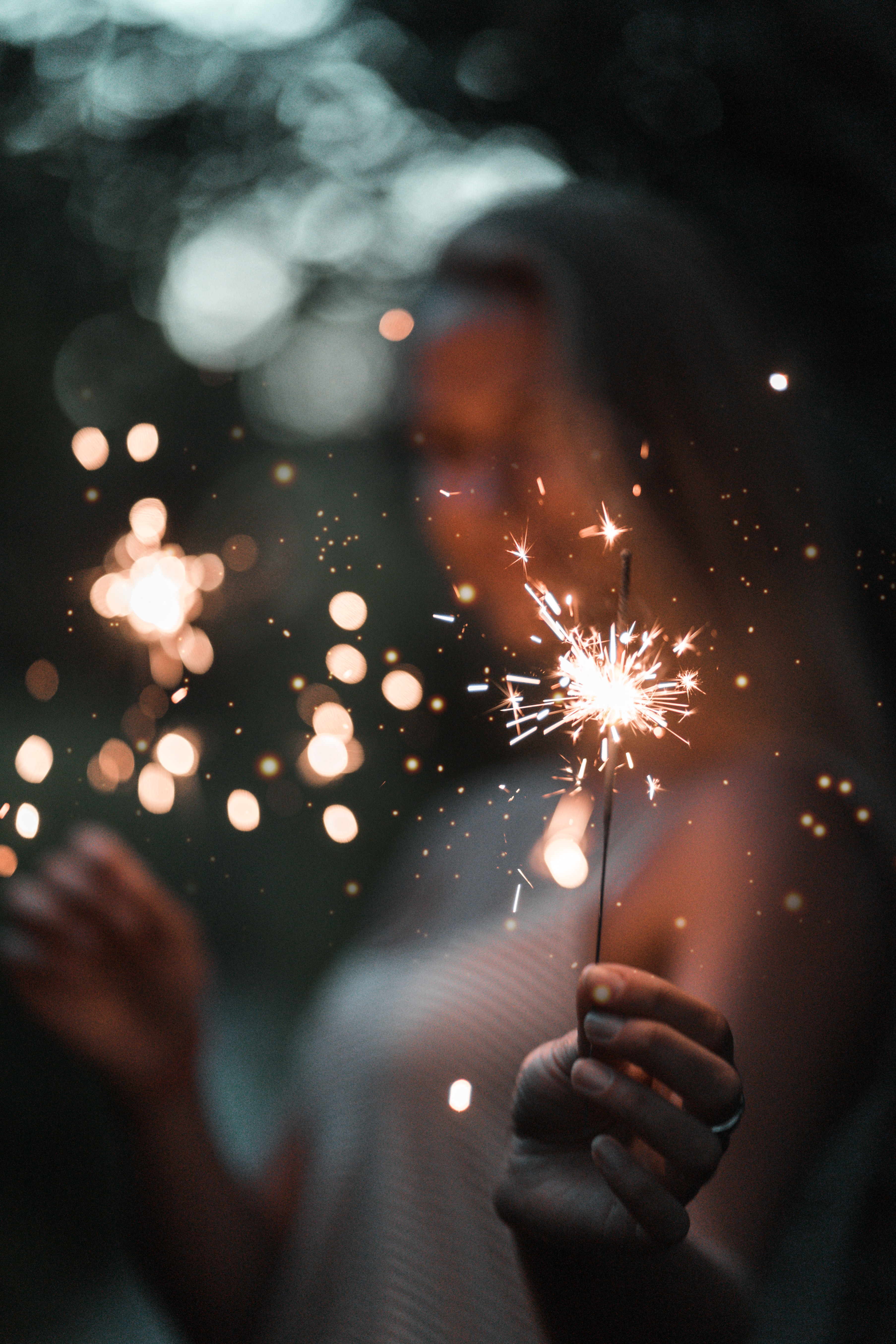 out of focus woman holding sparklers to camera
