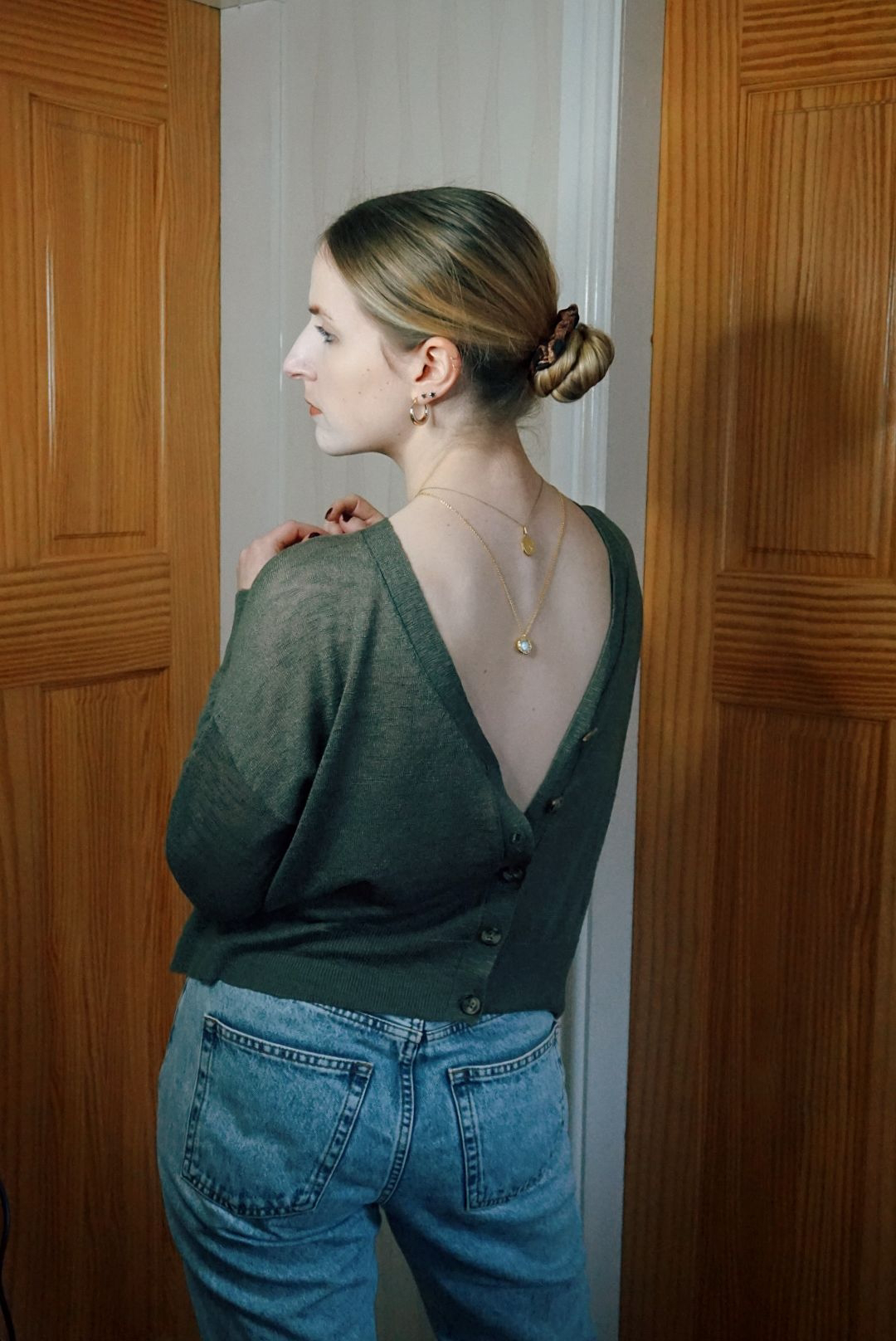 Amy facing away from camera, wearing a cardigan and two necklaces back to front