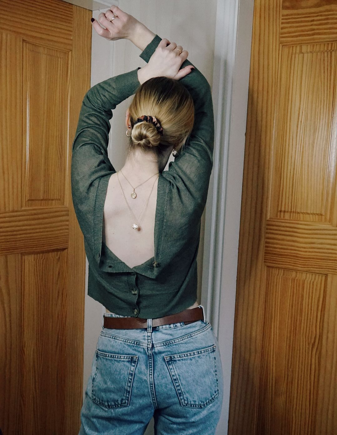 Amy with her hands in the air, back to the camera wearing a cardigan and two gold necklaces back to front