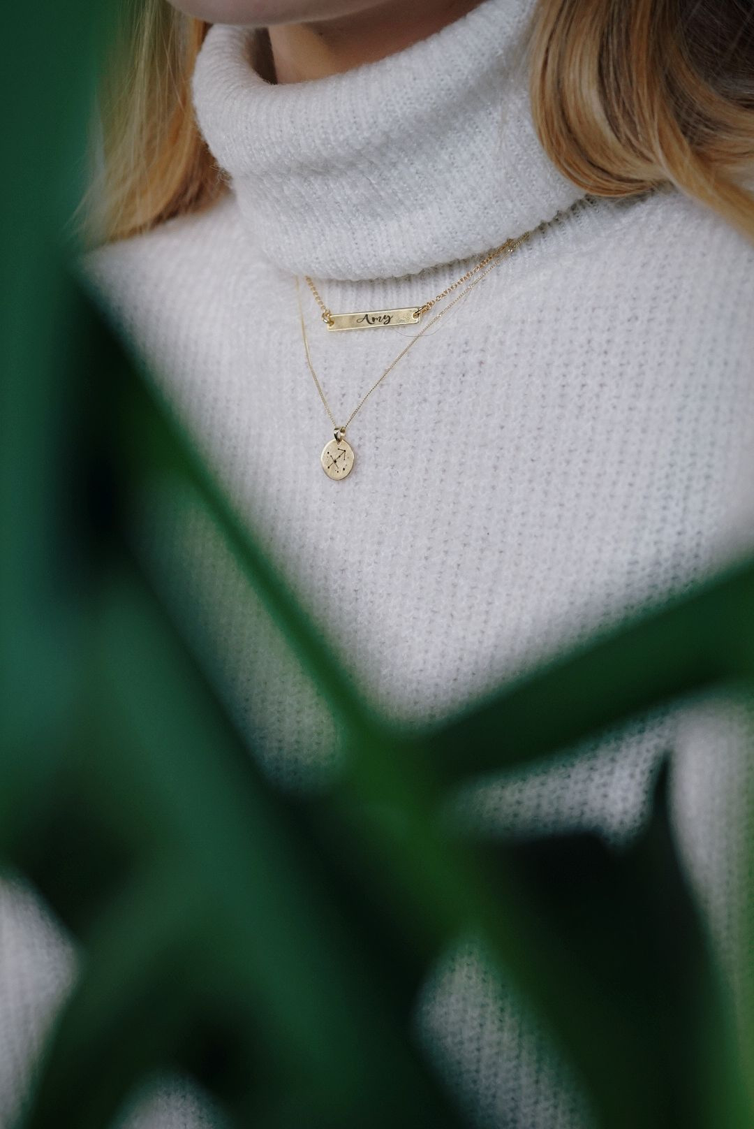 close up of girl wearing two necklaces, one is a gold bar necklace, the other a pendant
