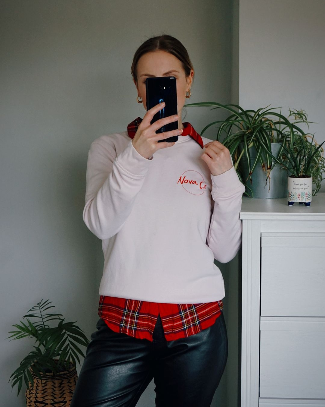 Amy is wearing a pink sweatshirt over a tartan shirt with black pleather trousers