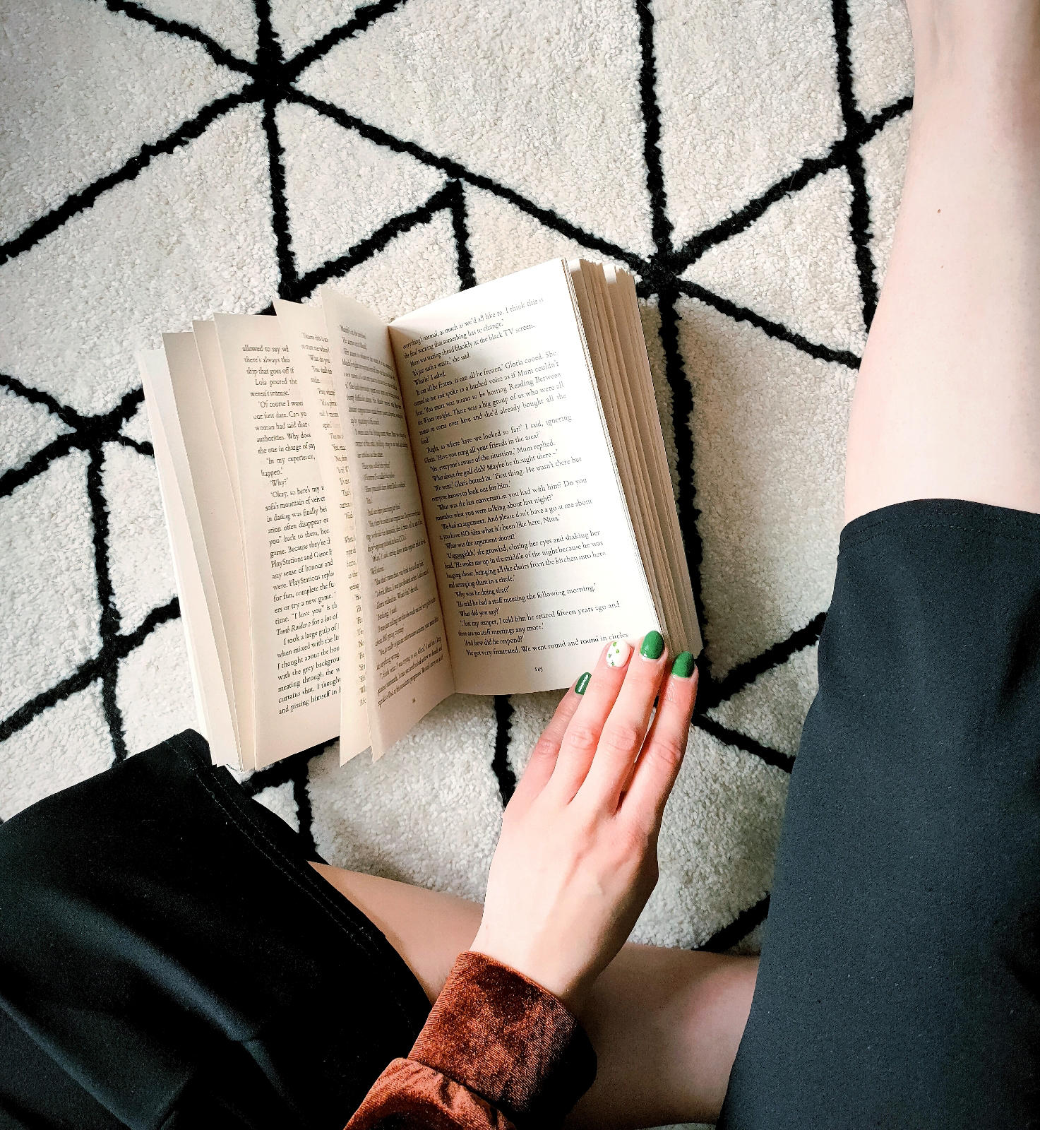 birds eye view of a book being held open on a black and white patterned rug