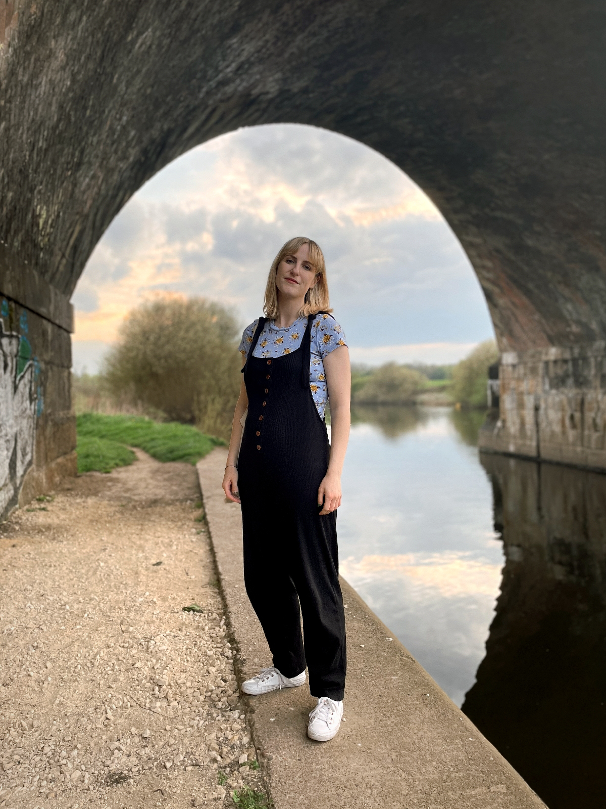 Outfit photo; wearing black cotton dungarees with tie straps over a short sleeved blue floral t-shirt with white trainers