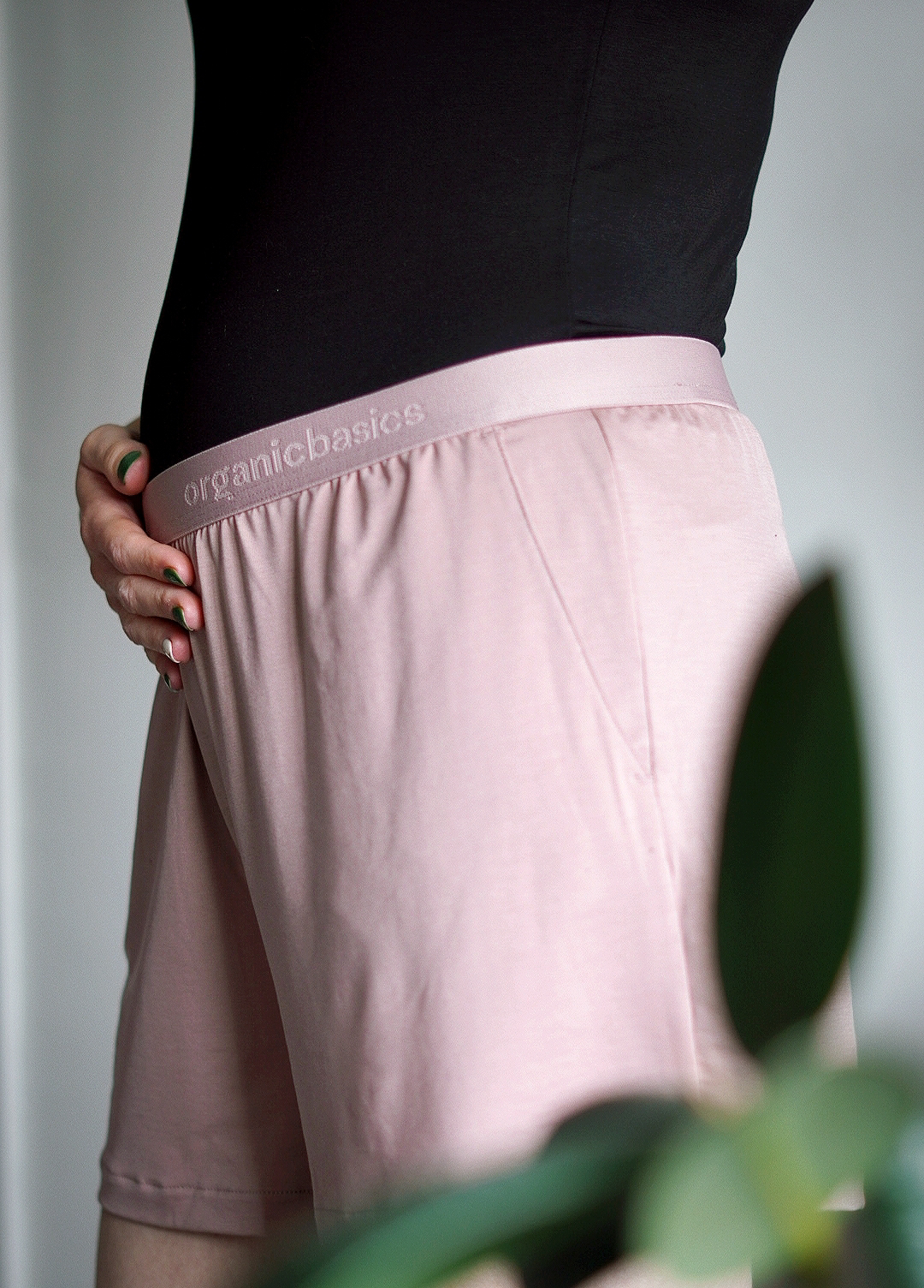 Outfit photo; close up of stomach from the side showing a small baby bump in a black tank top with pale pink shorts on the bottom