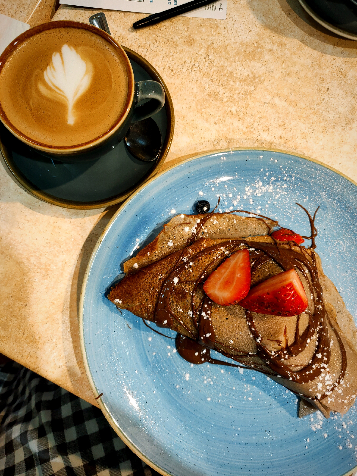 birds eye view of a folded over crepe covered in nutella and strawberries and a flat white next to it