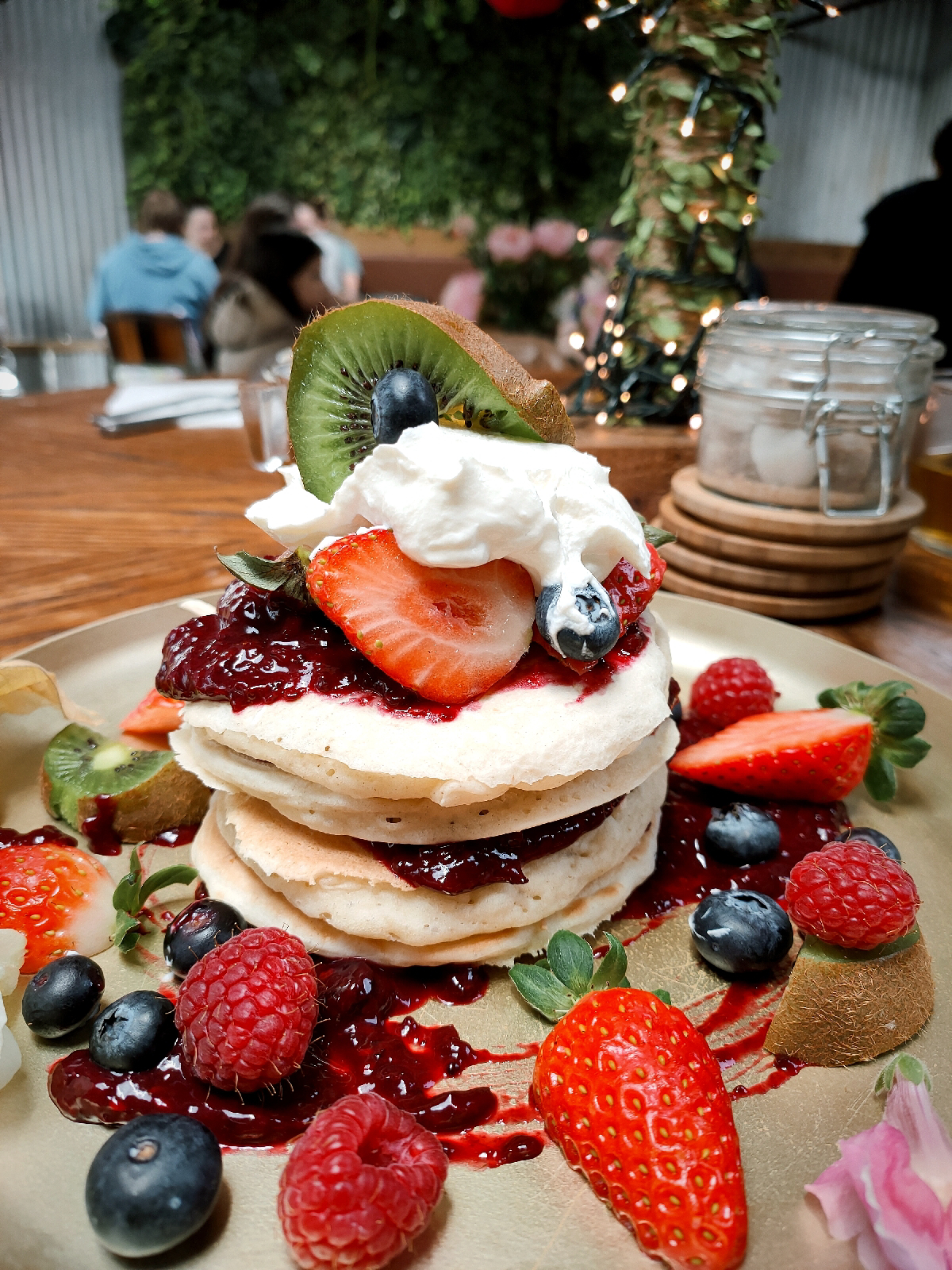 a big stack of pancakes covered in natural yogurt and mixed berries on a restaurant table