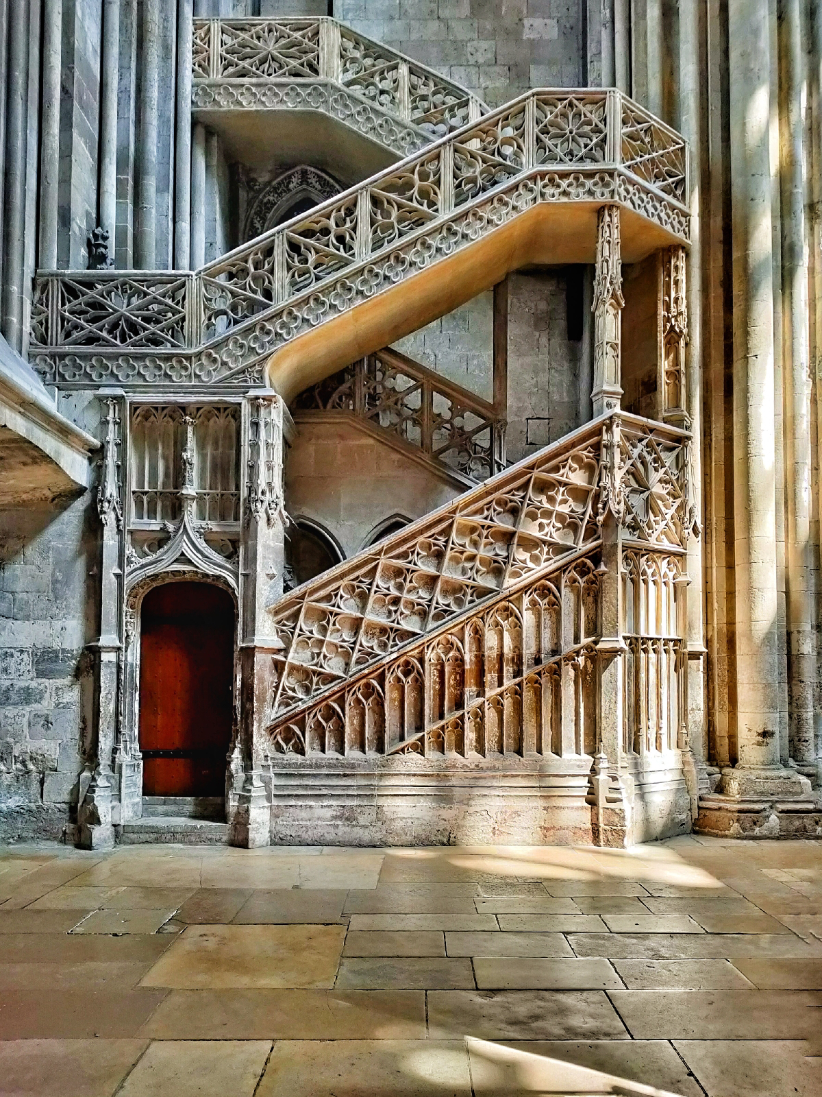 interior of a cathedral showing a staircase where light is shining onto part of it through huge windows