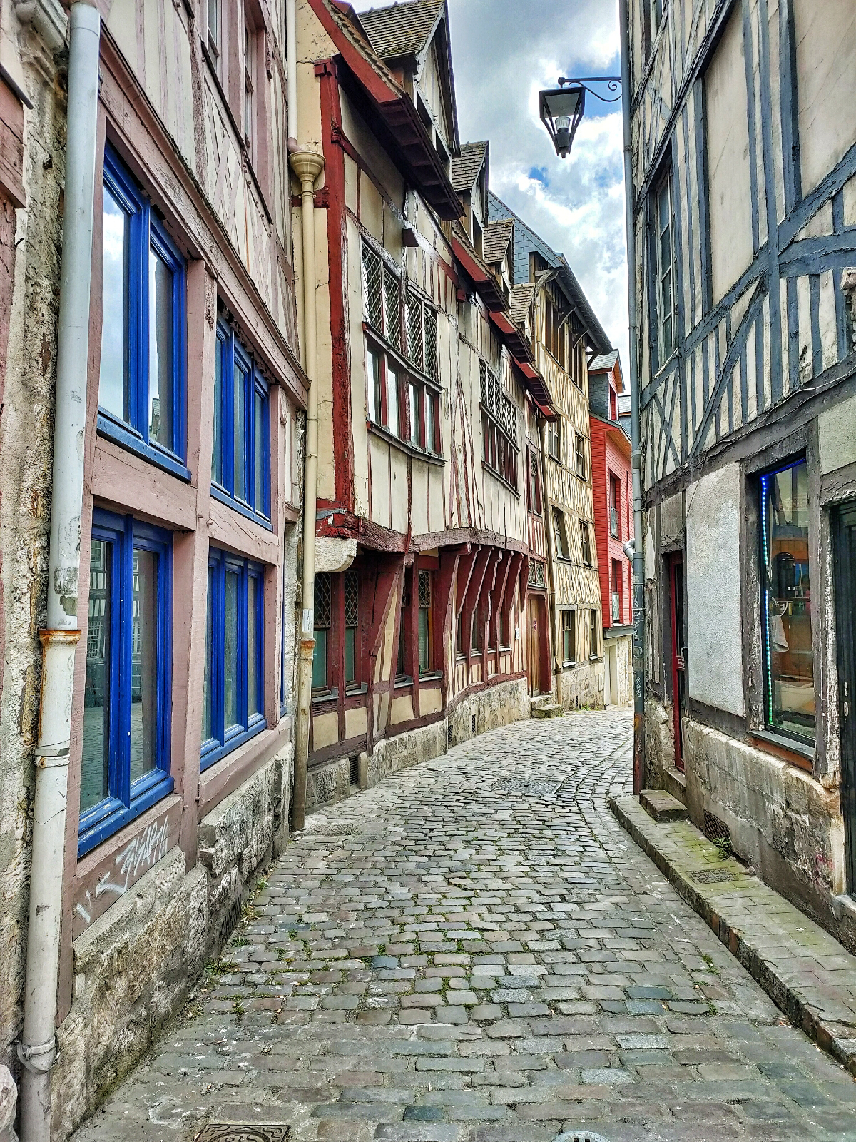 view down a cobbled street of wonky and rickety looking striped houses with shutters on the windows