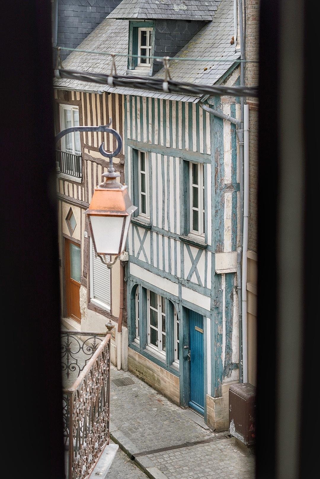 view out of a window down a French street with lanterns and a blue striped house in view