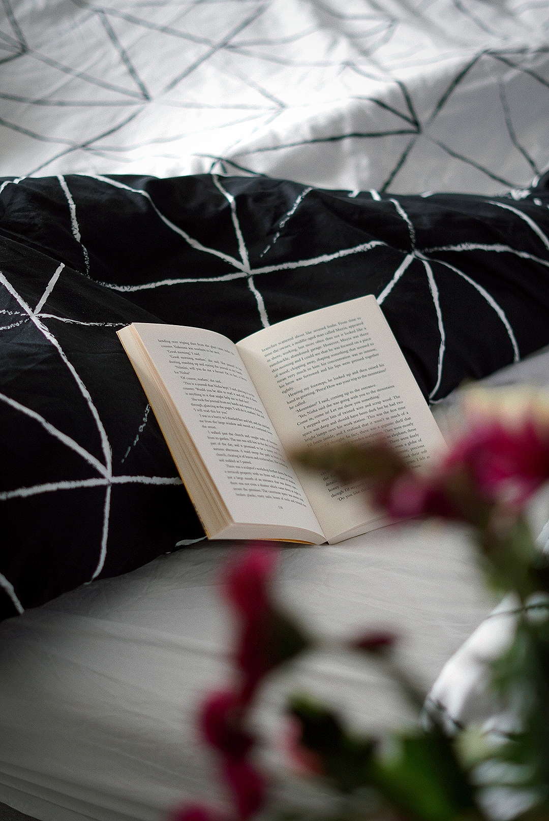 a book lies open on black and white geometric patterned bedcovers