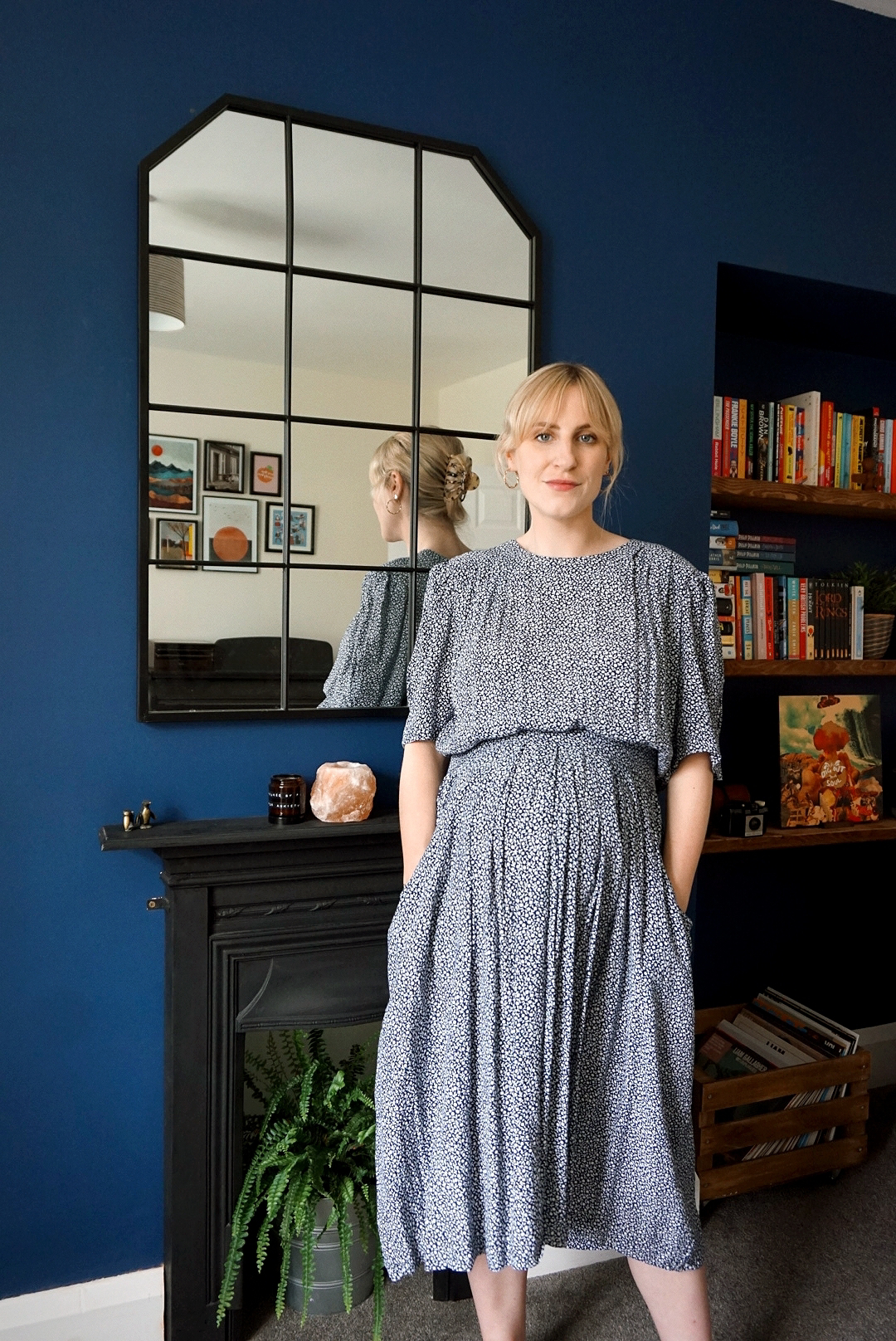 Outfit photo: Amy is stood in her living room wearing a floaty blue floral midi dress. She has her hands in her pockets.