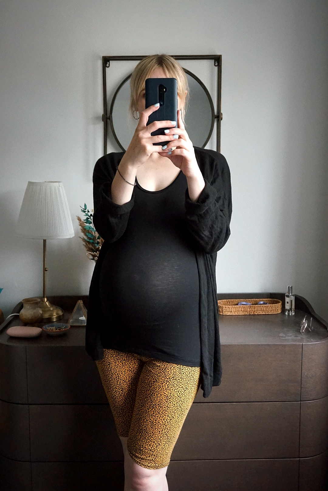 Outfit photo: Amy is taking a selfie showing her outfit; leopard print cycling shorts, a black vest top and a black cardigan