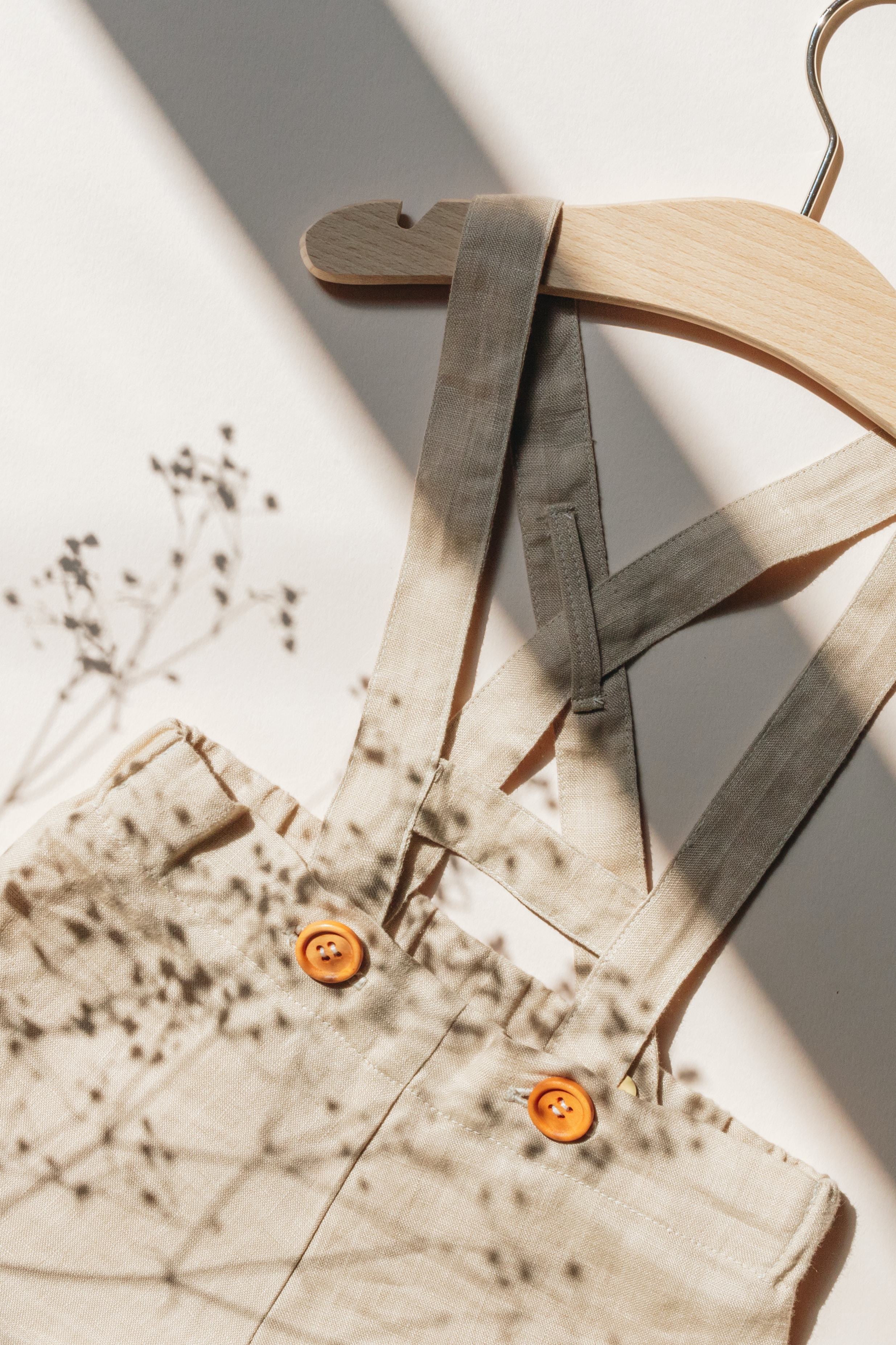 flatlay of a baby's neutral coloured dungarees on a hanger with some gypsophila laid next to them