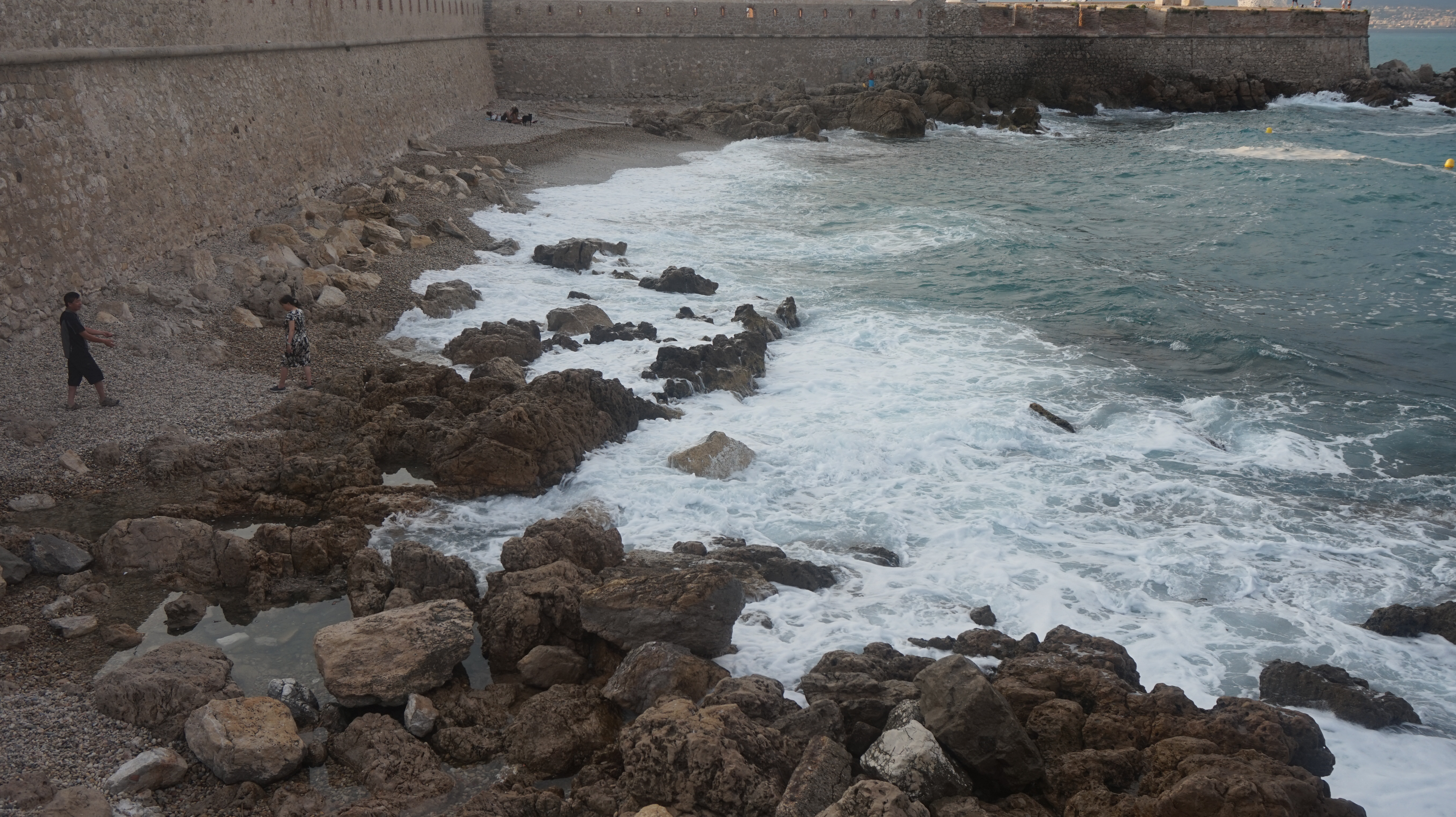 a rocky beach surrounded by high walls, looking out to a blue sea