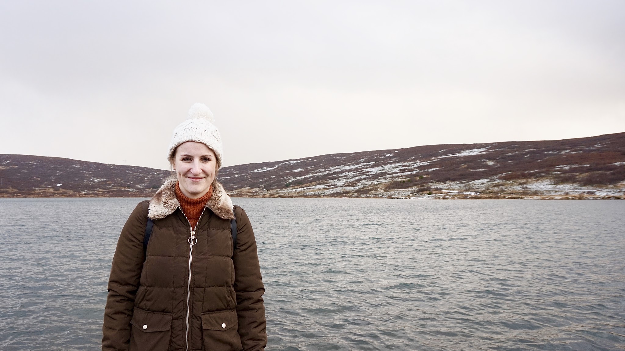 smiling woman in a bobble hat in front of a lake