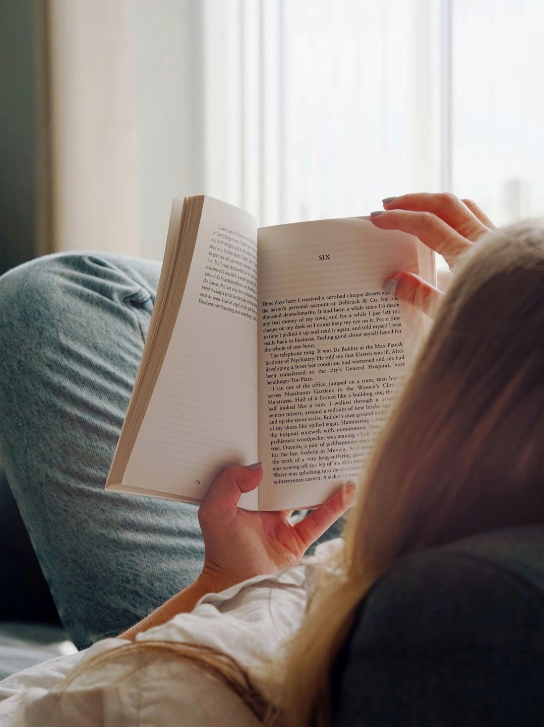 woman laid on sofa reading a book