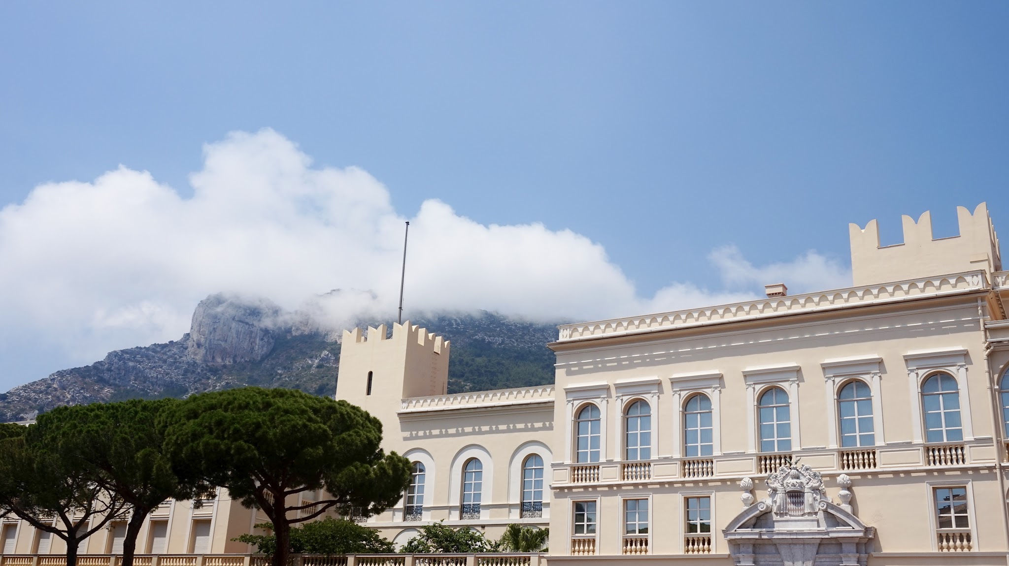 a yellow coloured palace building, with mountains in the background, a blue cloudy sky