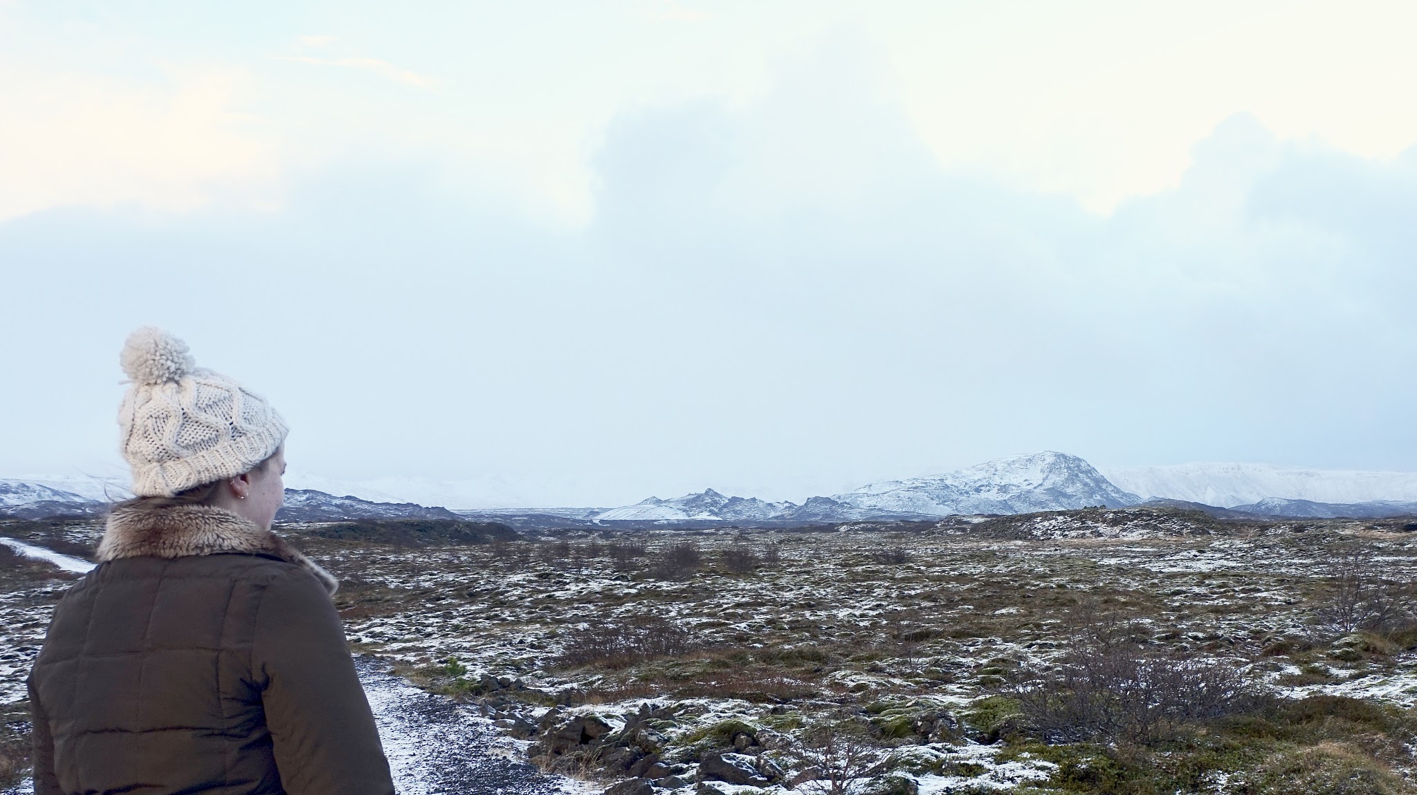 woman in bobble hat looking out onto snowy mountains